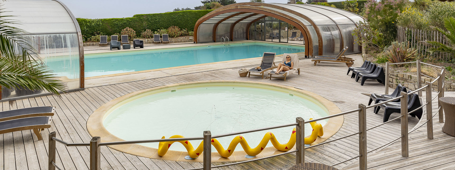 Femme allongée sur une chaise longue en lisant un livre devant une pataugeoire 