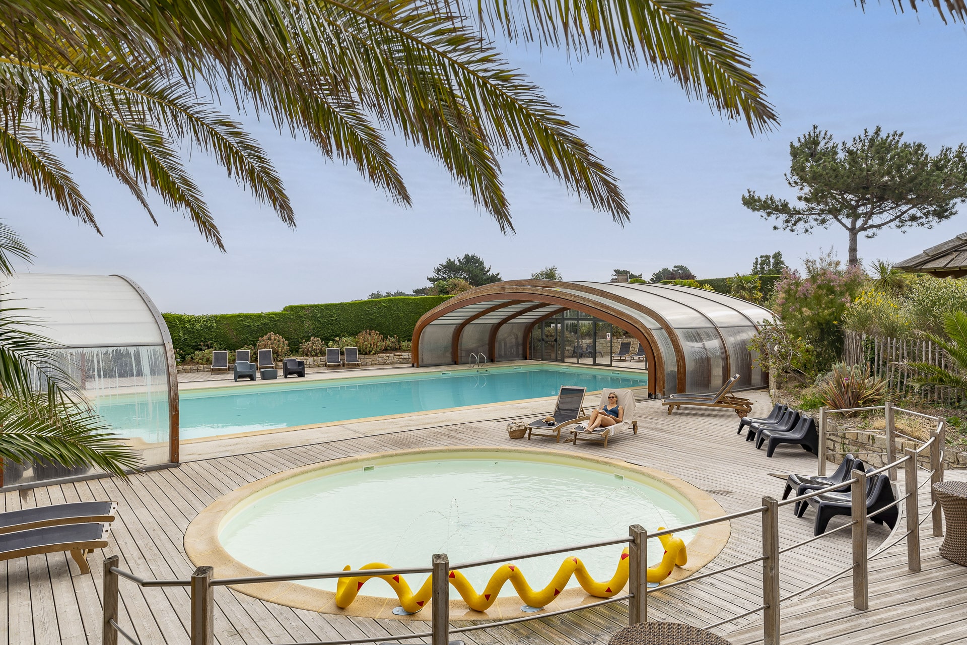 Piscine avec terrasse en bois et palmiers.
