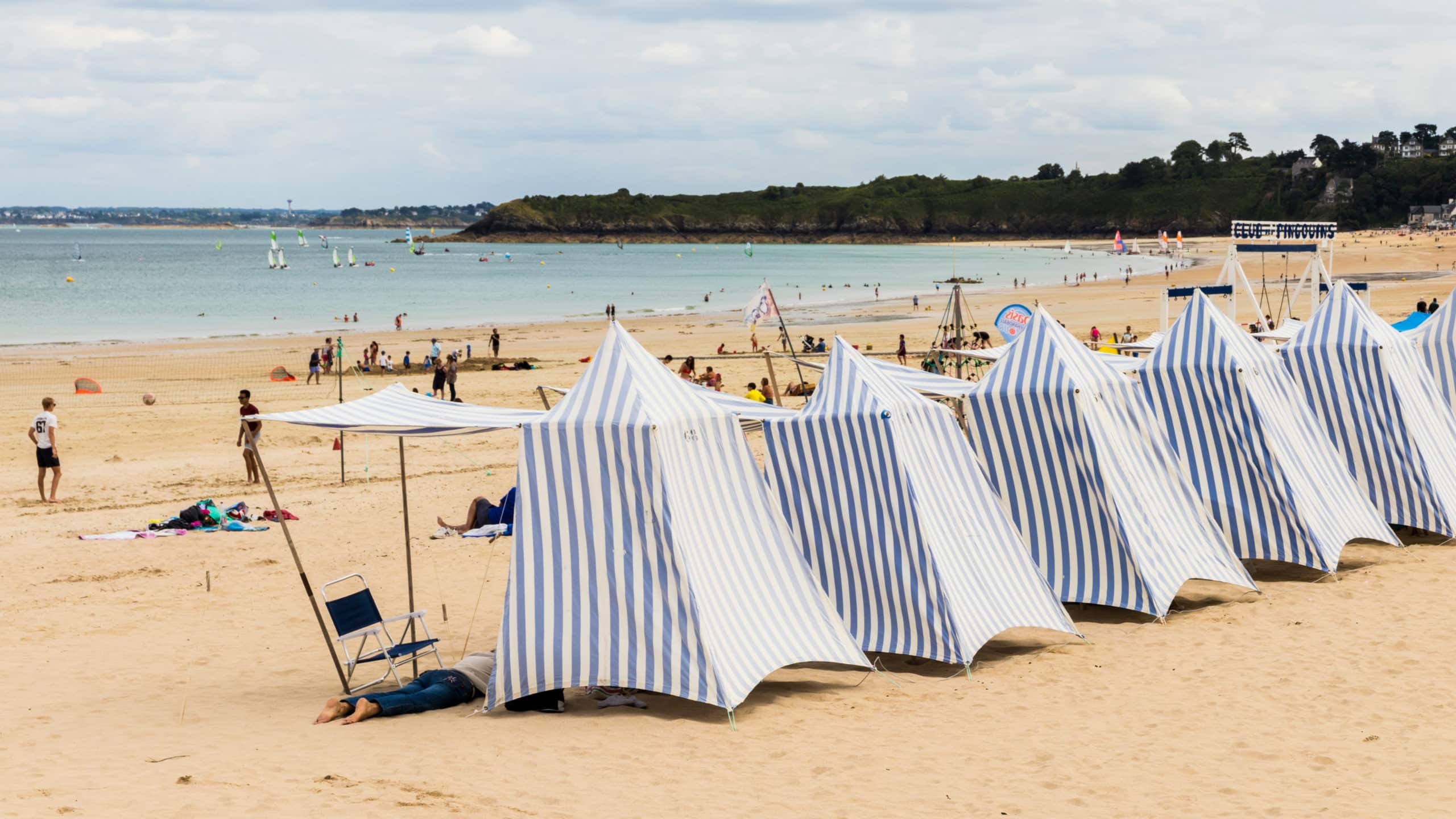 Plage avec tentes rayées et mer en arrière-plan.