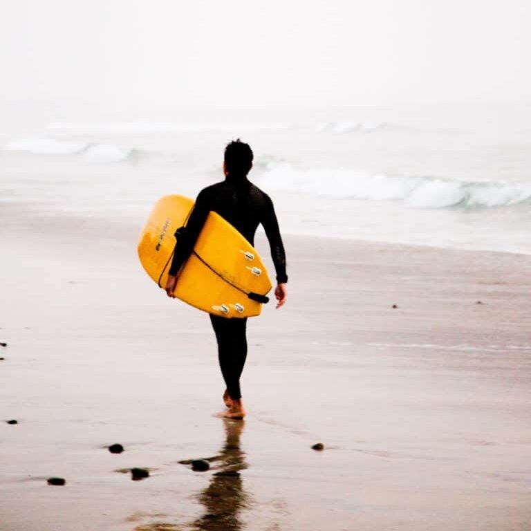 Surfeur marchant sur la plage avec une planche jaune.
